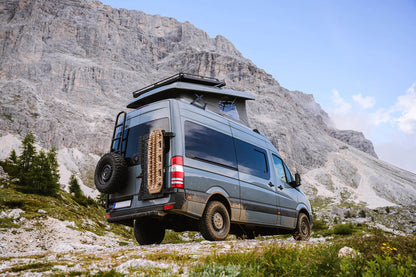 Offroad-Van mit montiertem Van-Gear-Fahrzeuganbauteil am Heck und Dachzelt vor Bergkette